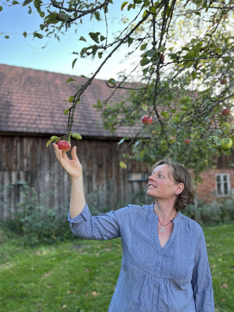 Ein Bild von Anja die einen Apfel von einem Apfelbaum pflückt